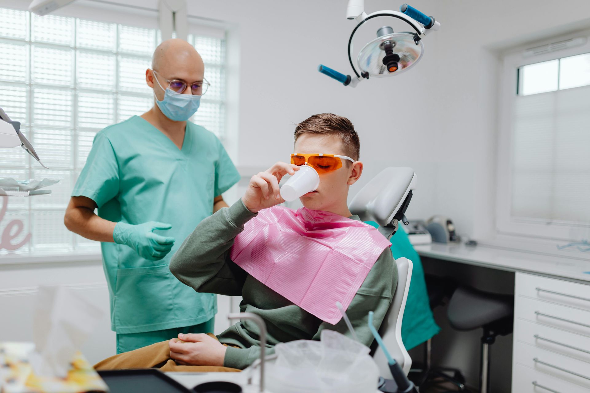 A man is sitting in a dental chair drinking from a cup.