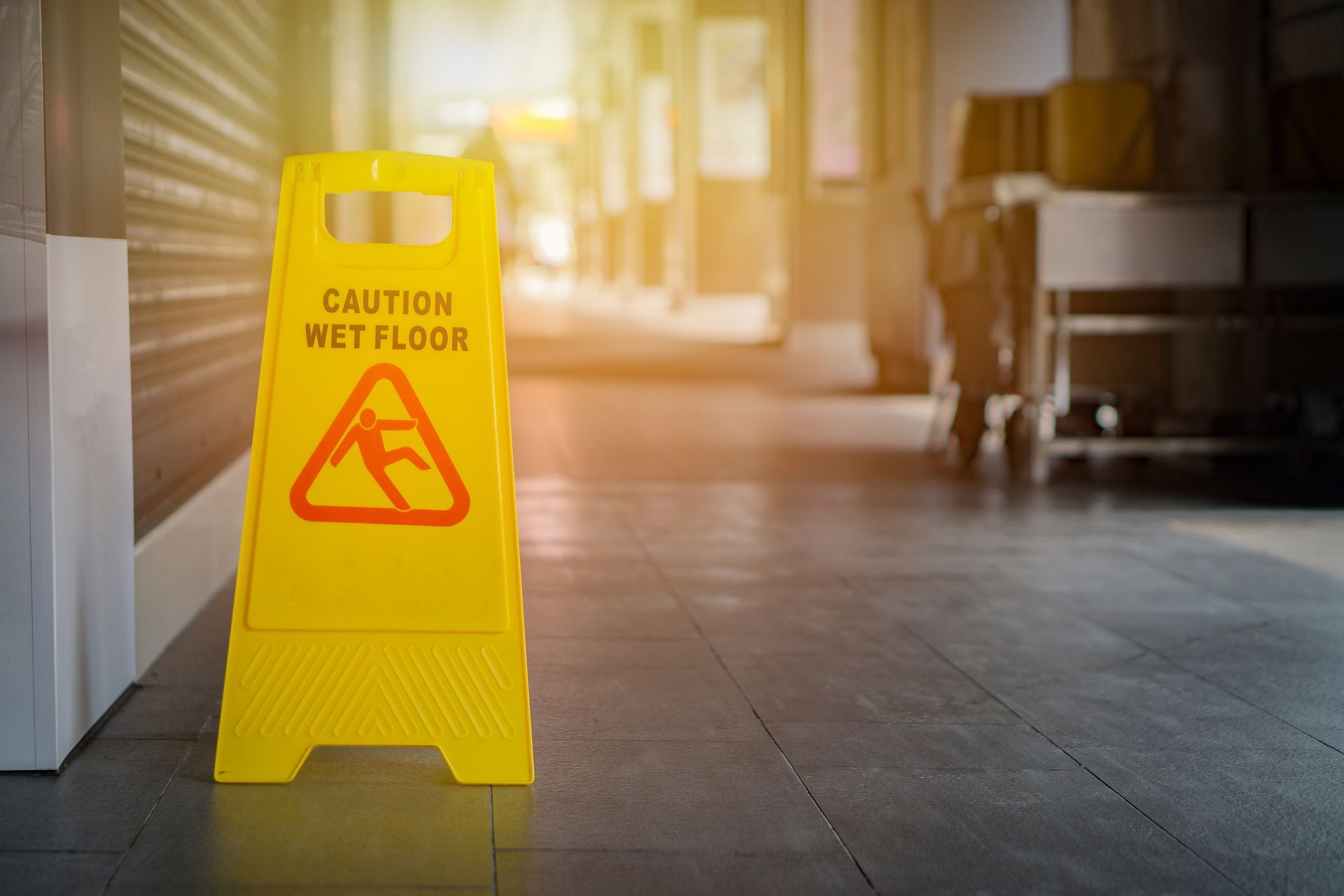 A yellow caution wet floor sign is sitting on a tiled floor in a hallway.