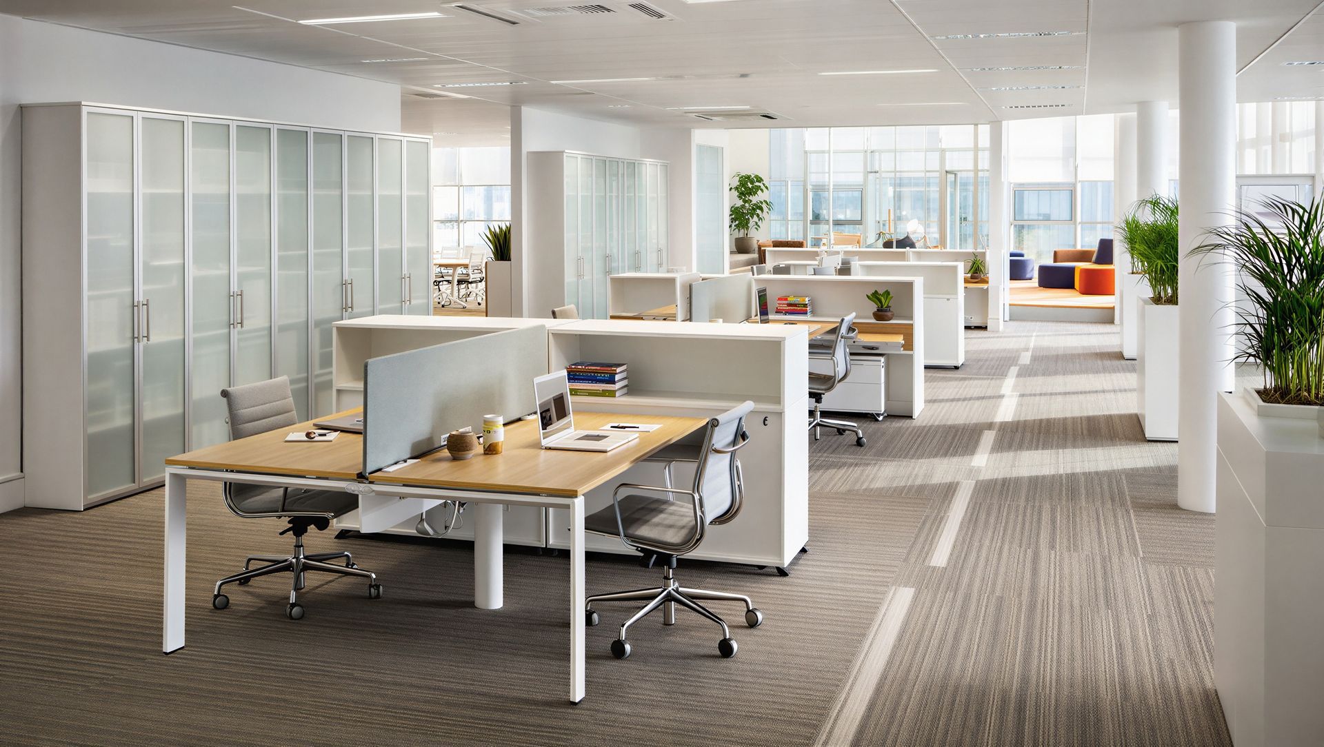 Modern open office with white desks, glass partitions, and empty swivel chairs under bright daylight