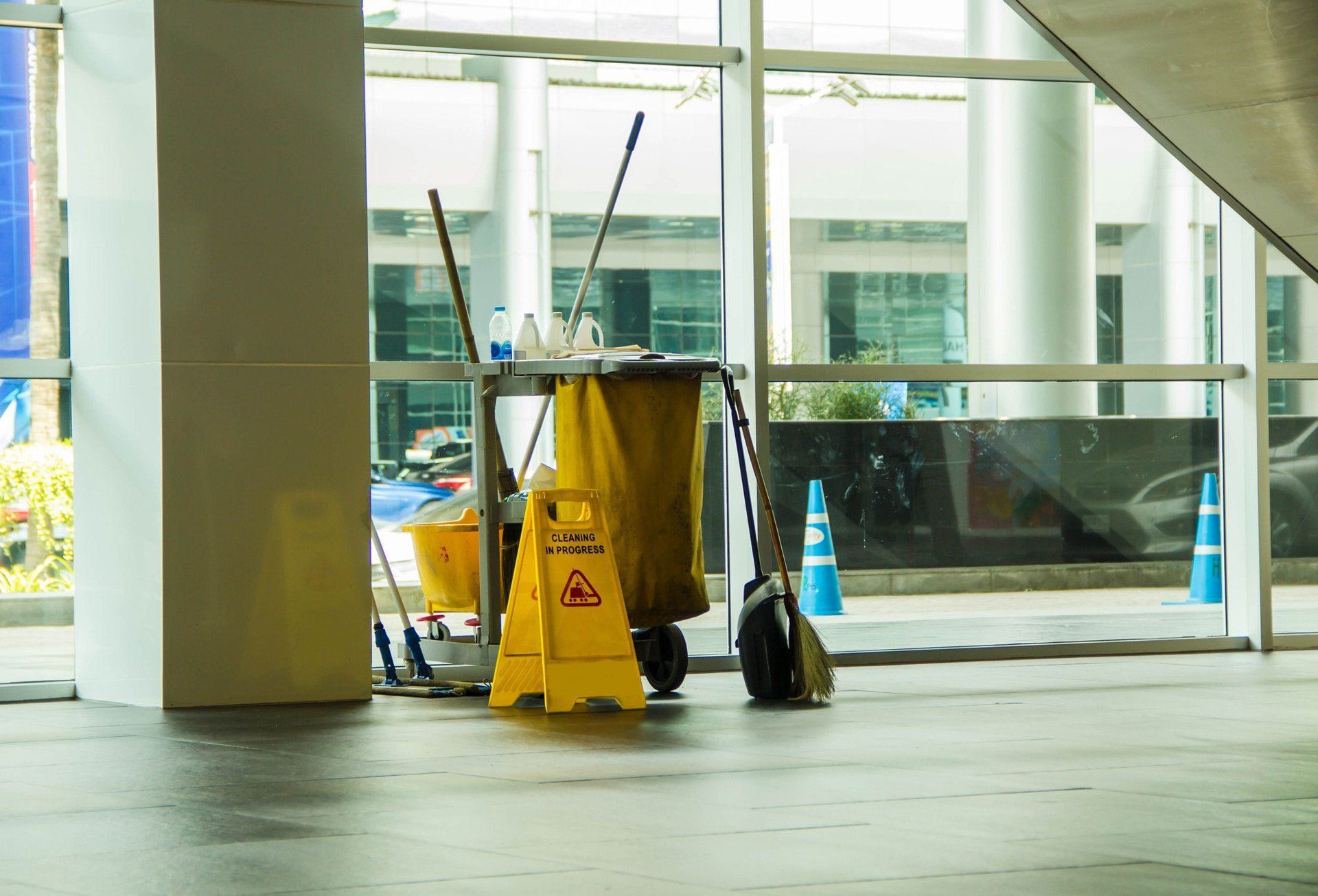 Yellow wet-floor sign and cleaning cart in a glass-walled lobby or terminal entrance