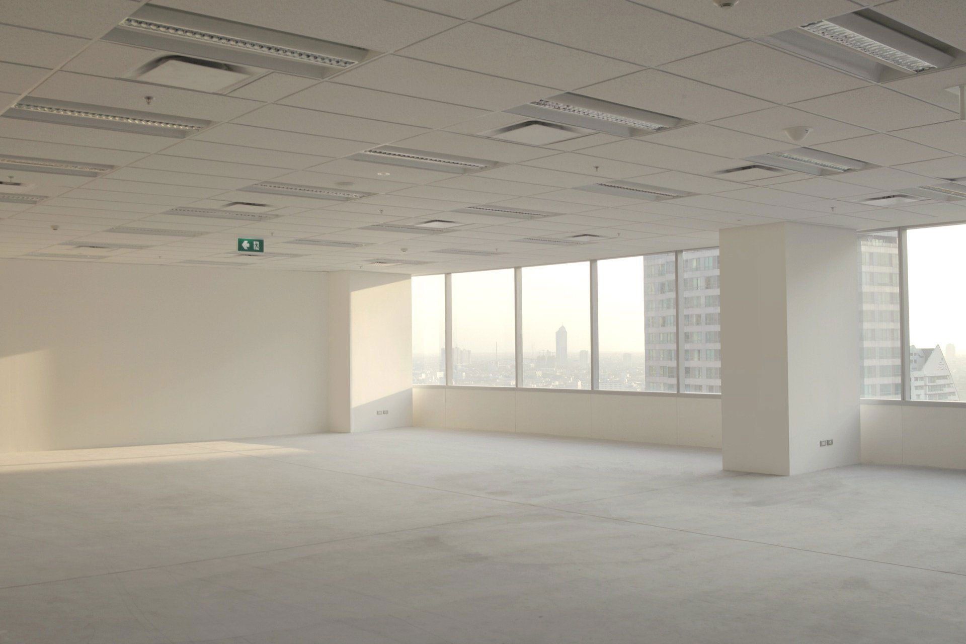 Empty unfurnished office space with white walls, carpet, and large windows letting in daylight