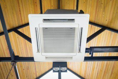 White ceiling air conditioner with open vents mounted on a wooden ceiling.