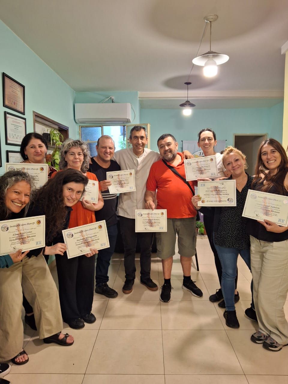Grupo de personas sosteniendo certificados, sonriendo en una habitación con paredes de color azul claro, celebrando un hito.