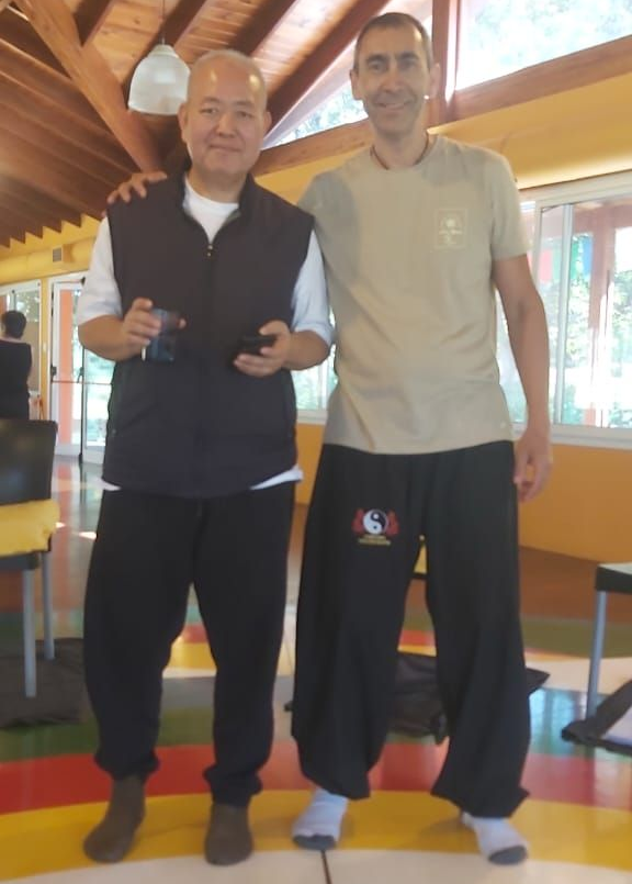 Dos hombres de pie, abrazados. Dentro de una habitación. Uno sostiene dos pequeños objetos negros.