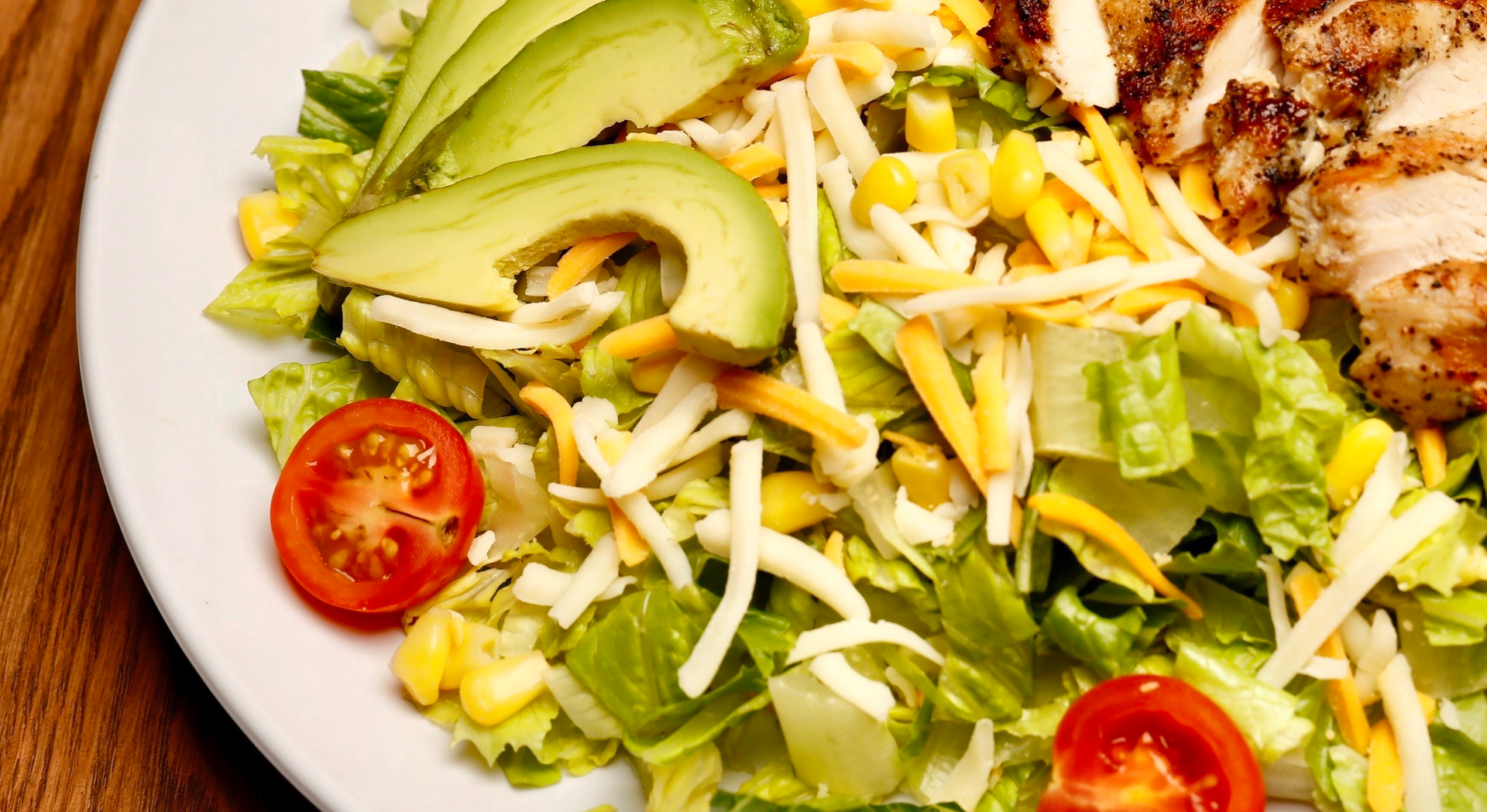 A salad with avocado, cheese , lettuce and tomatoes on a plate.