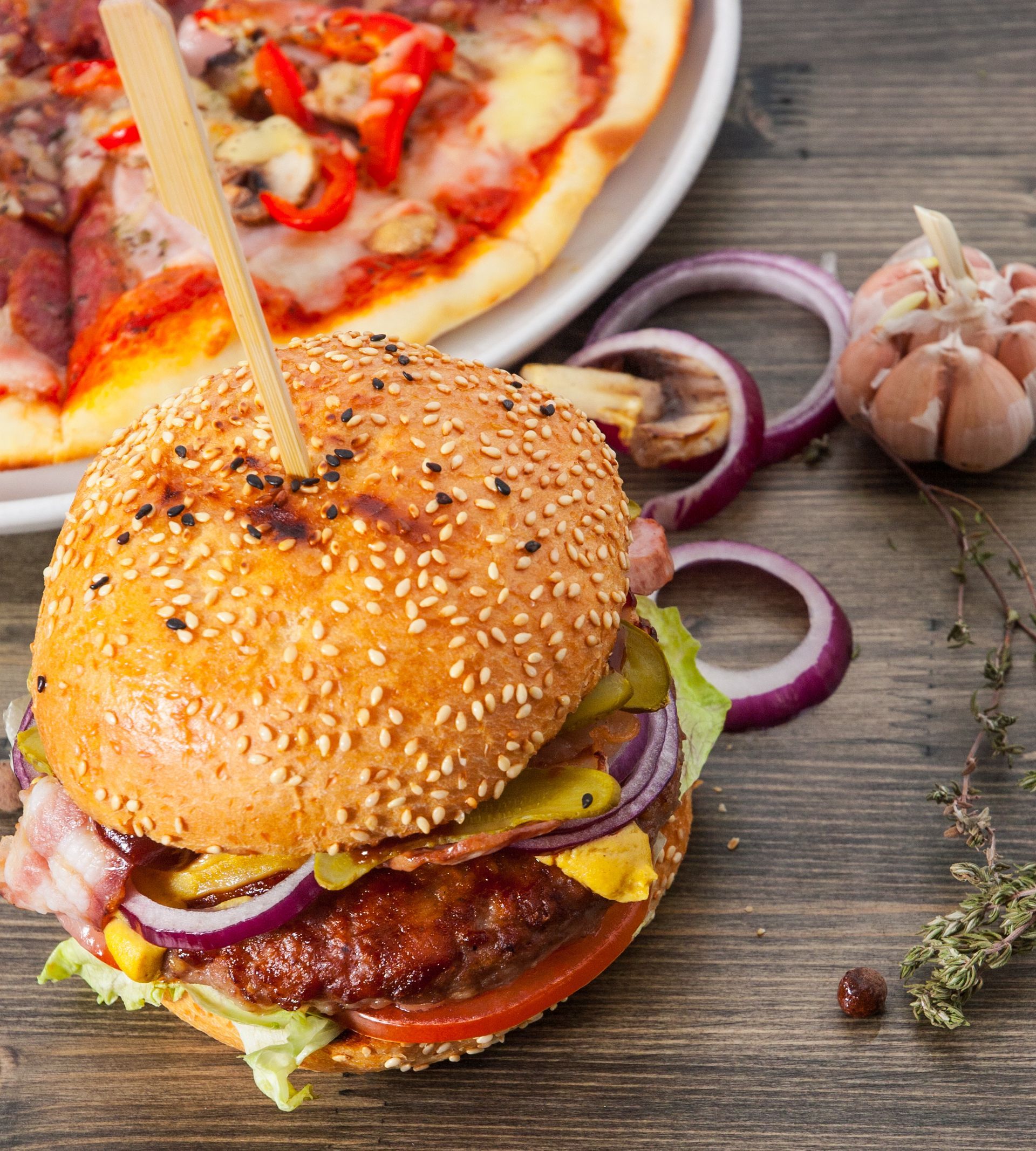 A hamburger is sitting on a wooden table next to a pizza
