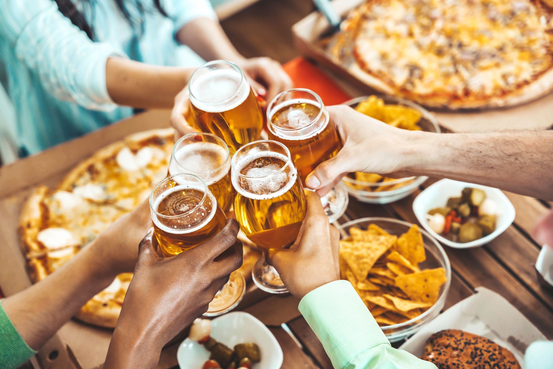 A group of people are toasting with beer and pizza.