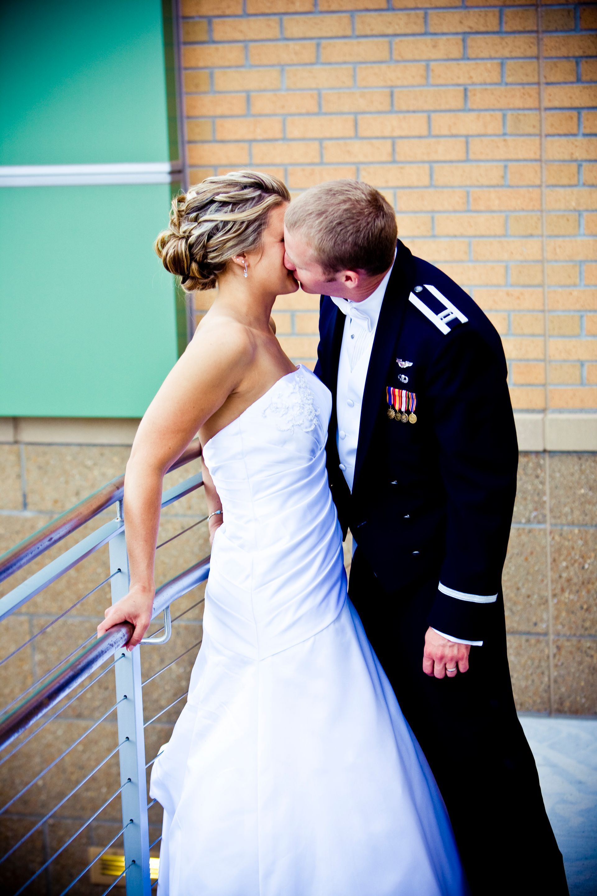 Bride in white dress kisses groom in military uniform.