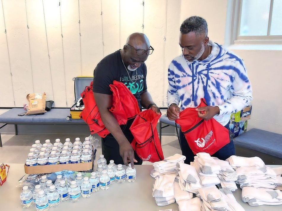 two men are standing around a table filled with water bottles and bags .