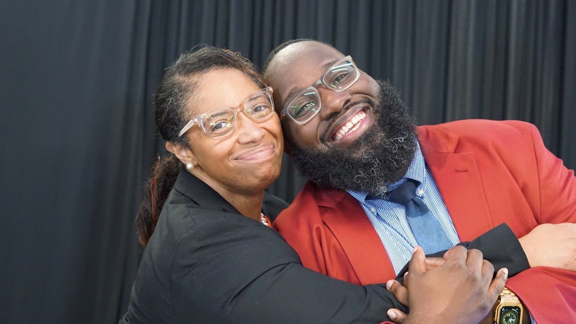 a man and a woman are hugging each other in front of a black curtain .