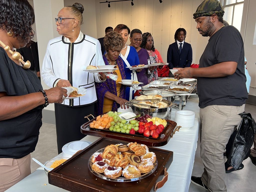 a group of people are standing around a table eating food .