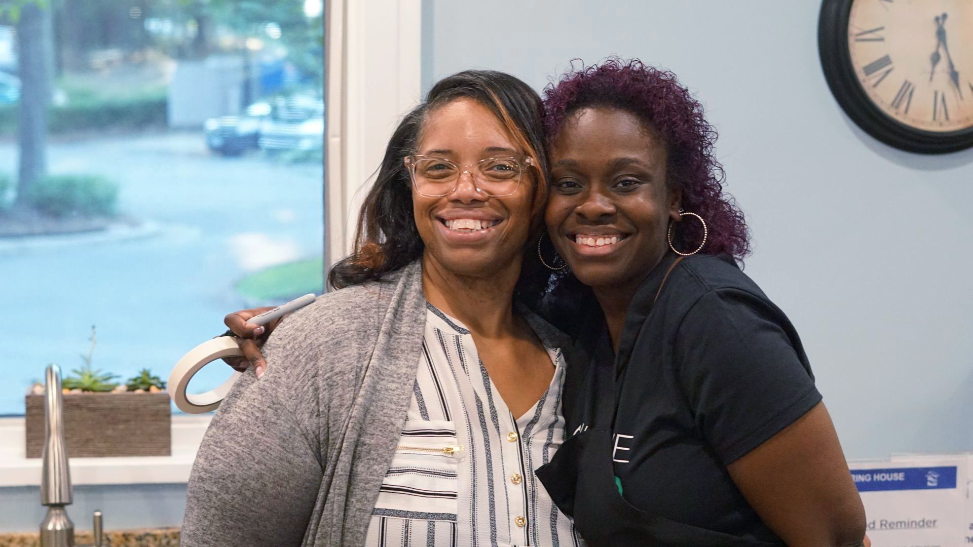 two women are posing for a picture in front of a clock .