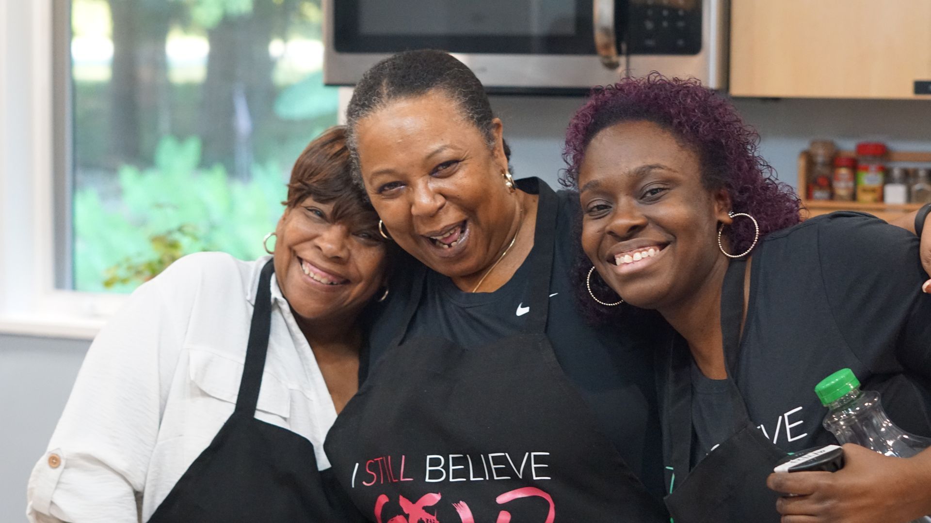 three women are posing for a picture in a kitchen .