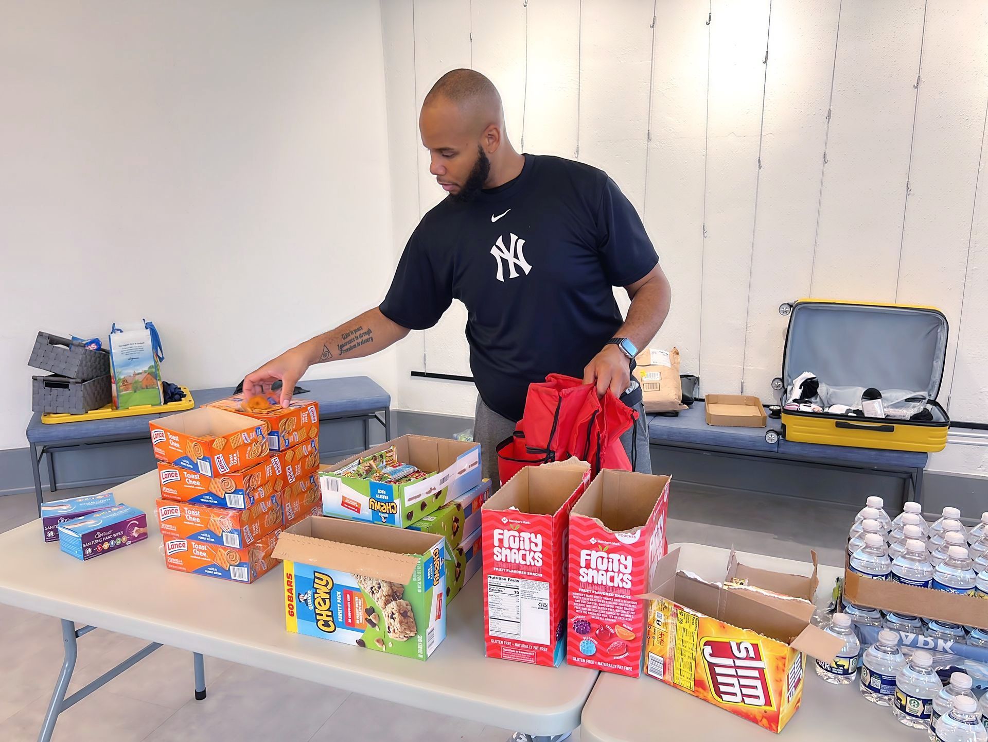 a man in a ny yankees shirt is arranging boxes of snacks on a table.
