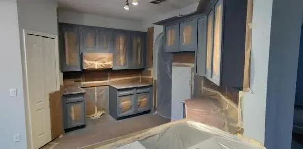 Kitchen undergoing renovation with gray cabinets and exposed walls.