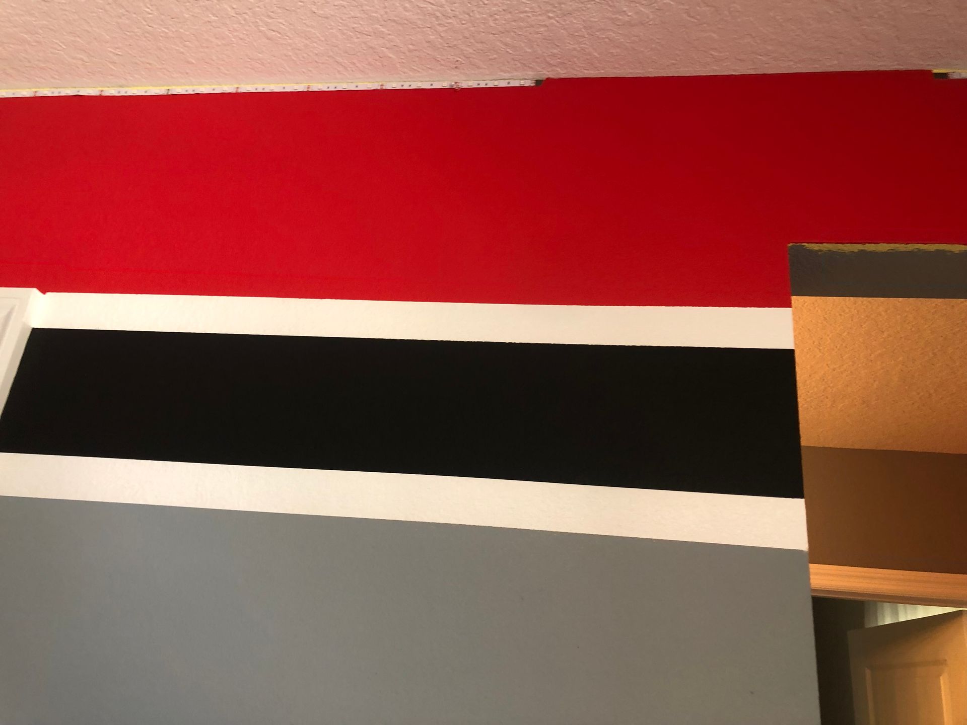 Red, white, black, and gray stripes painted on a wall, with a glimpse of a brown cabinet.