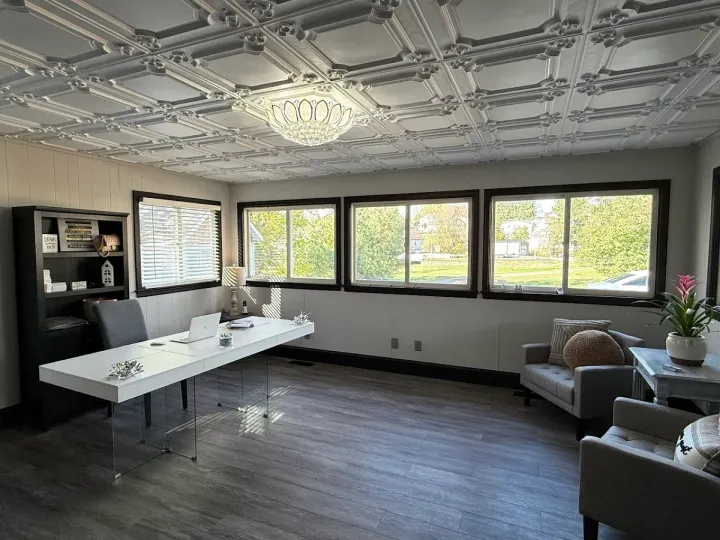 An office with a white desk, grey seating, large windows, and a decorative ceiling.