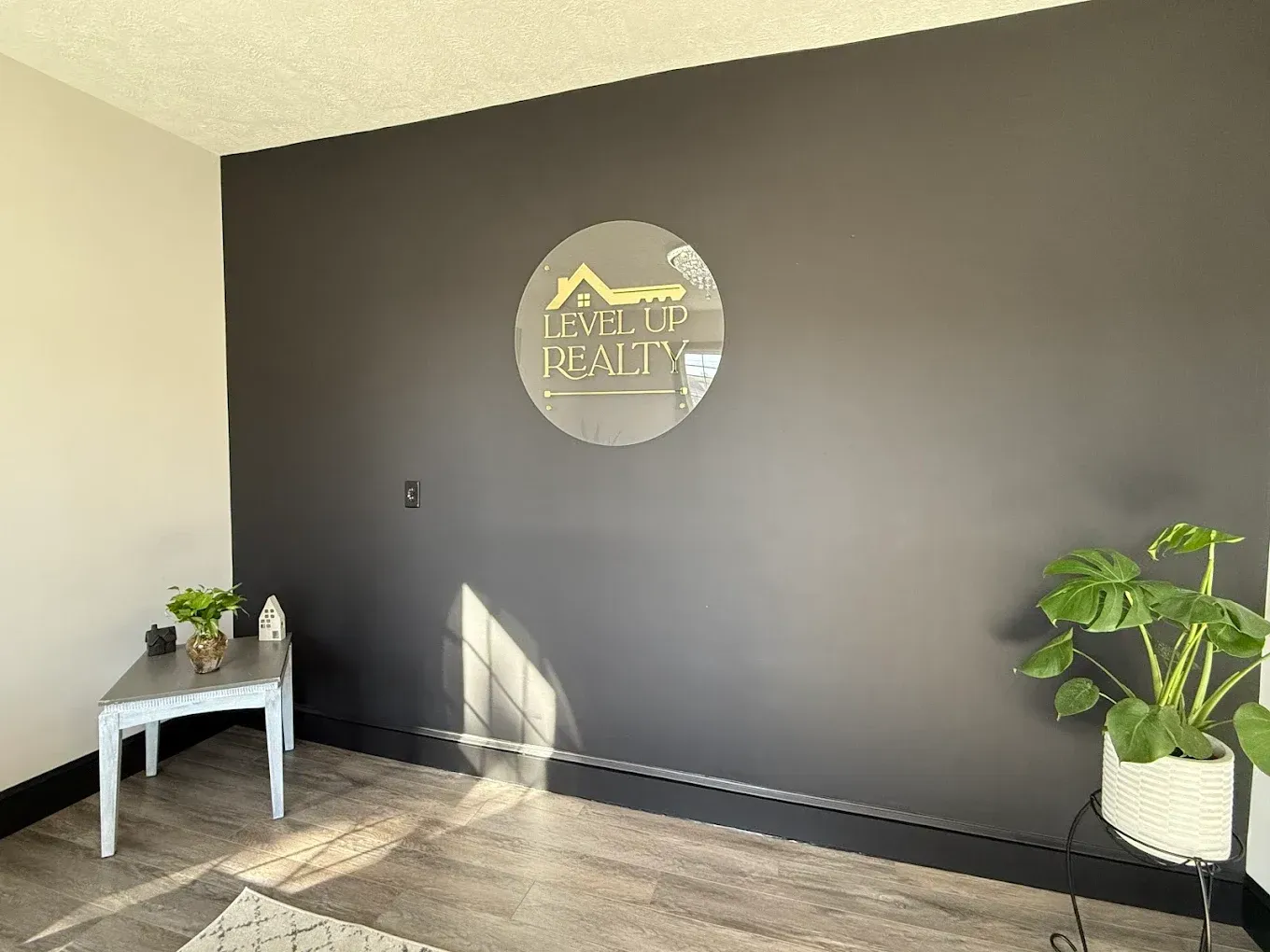 Dark gray wall with a gold logo, small chair, and potted plant.