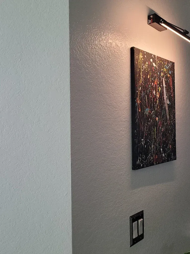 Gray wall with artwork and light fixture, illuminated from above.