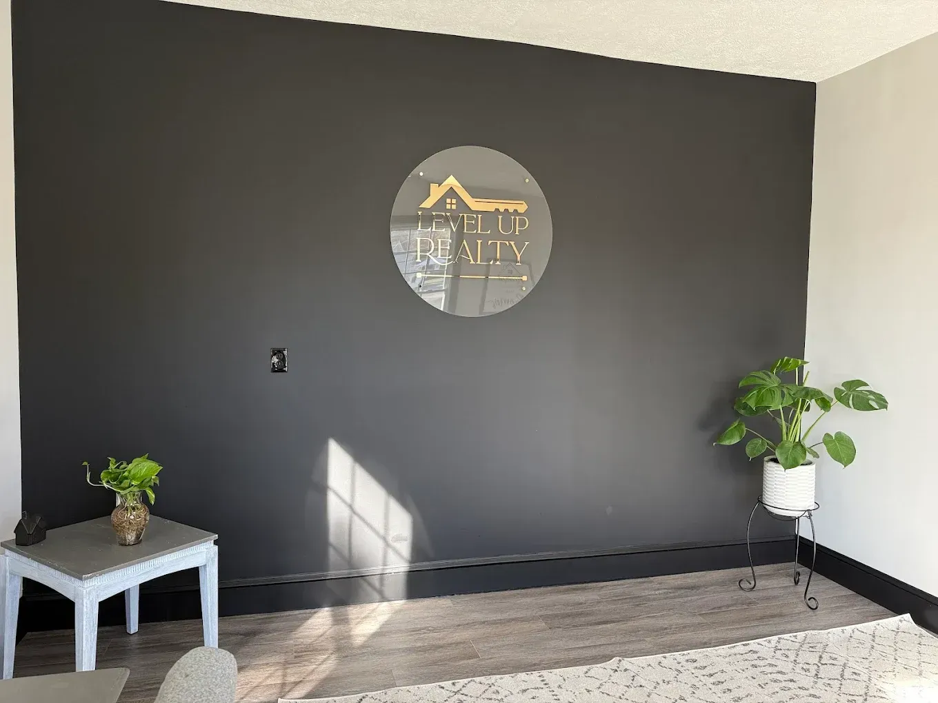 Black accent wall with real estate logo, small table with flowers, potted plant.