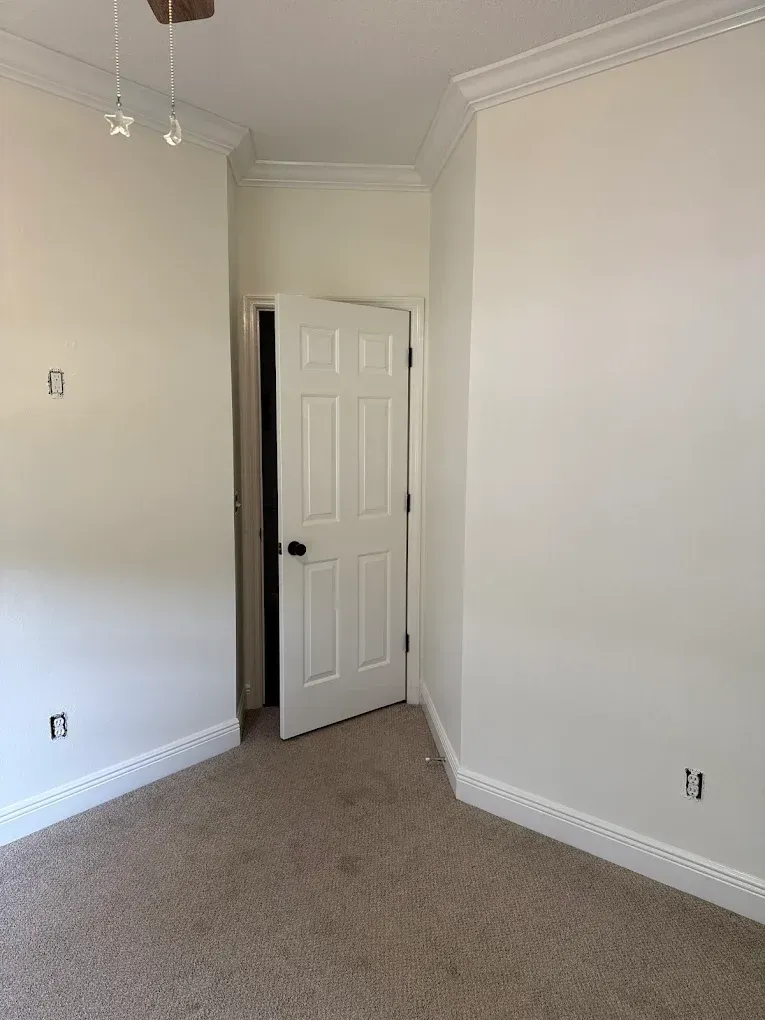 Empty room with white walls, door, and tan carpet.