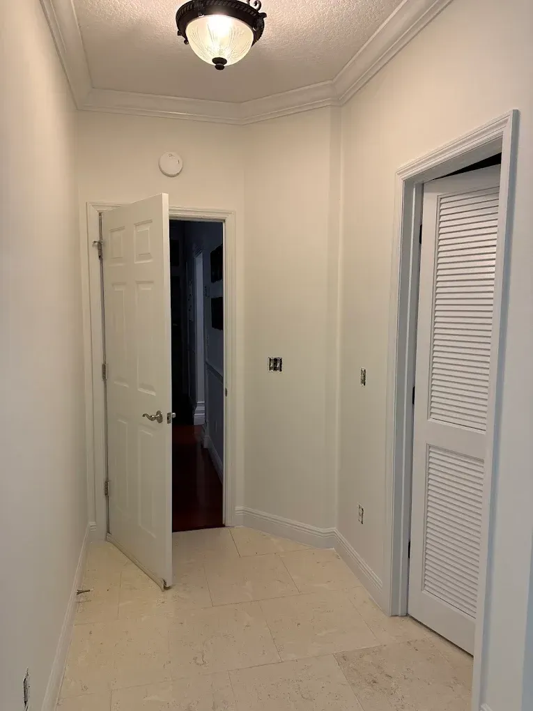 Narrow hallway with white walls, doors, and trim, and a central light fixture.