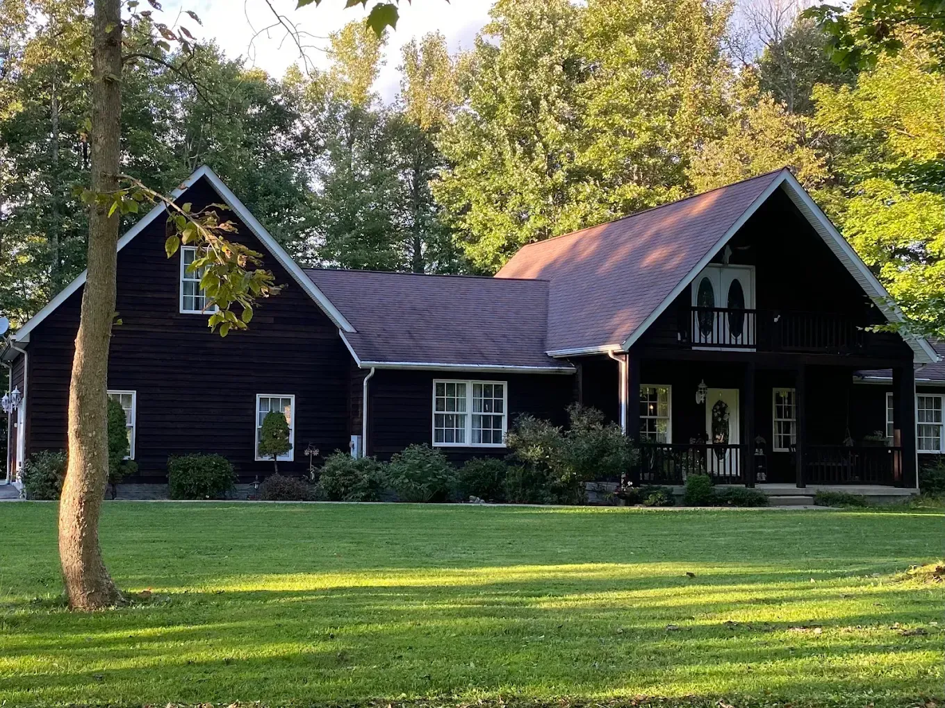 Dark-colored house with a green lawn, trees in the background.