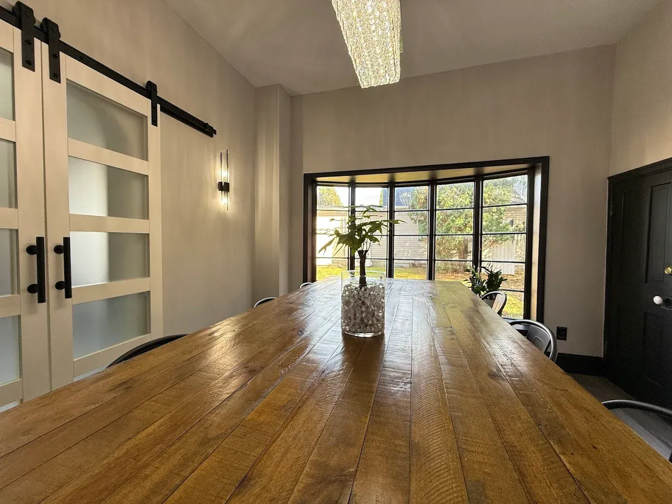 A long wooden table in a meeting room with a view to the outdoors, flanked by doors and a window.