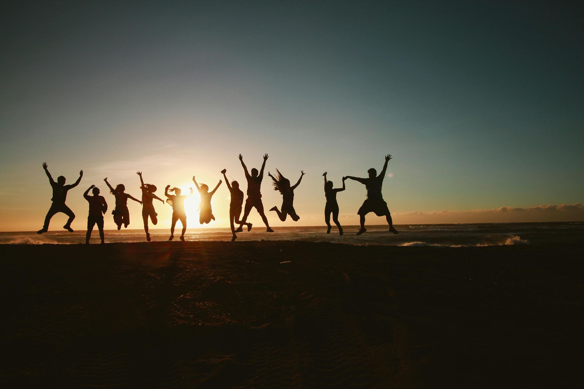 Group of people jumping and celebrating together on a beach at sunset, symbolizing teamwork, joy, and connection.