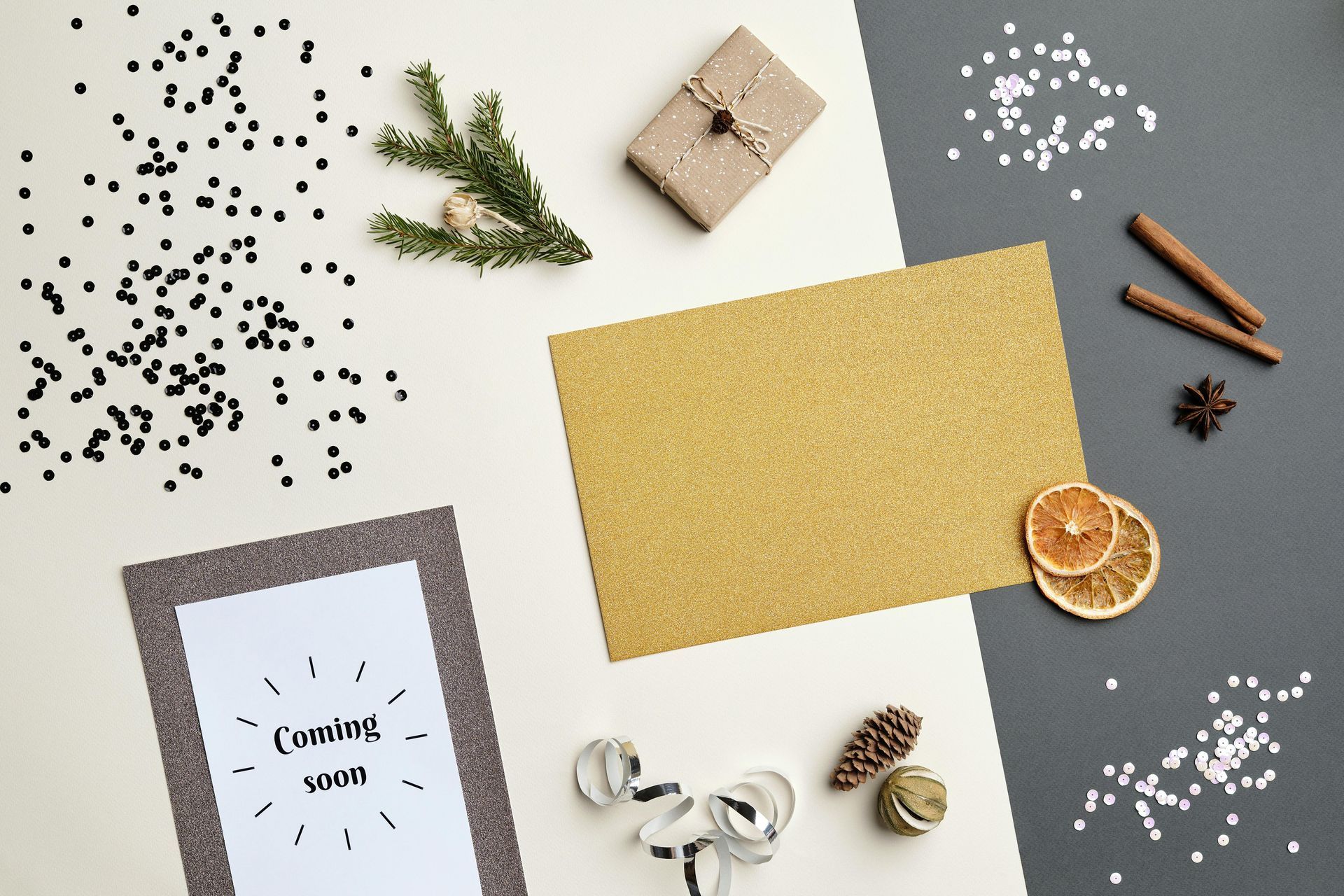 Flat lay of festive items including a ‘Coming Soon’ card, gold paper, dried oranges, cinnamon sticks, and winter decor.