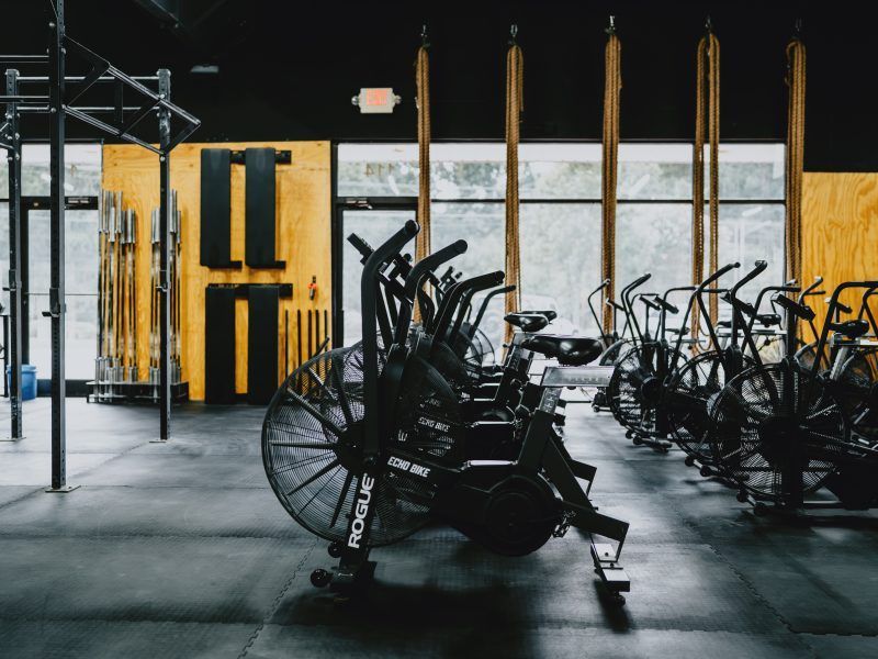 Indoor gym with rows of exercise bikes and a few weight machines near large windows