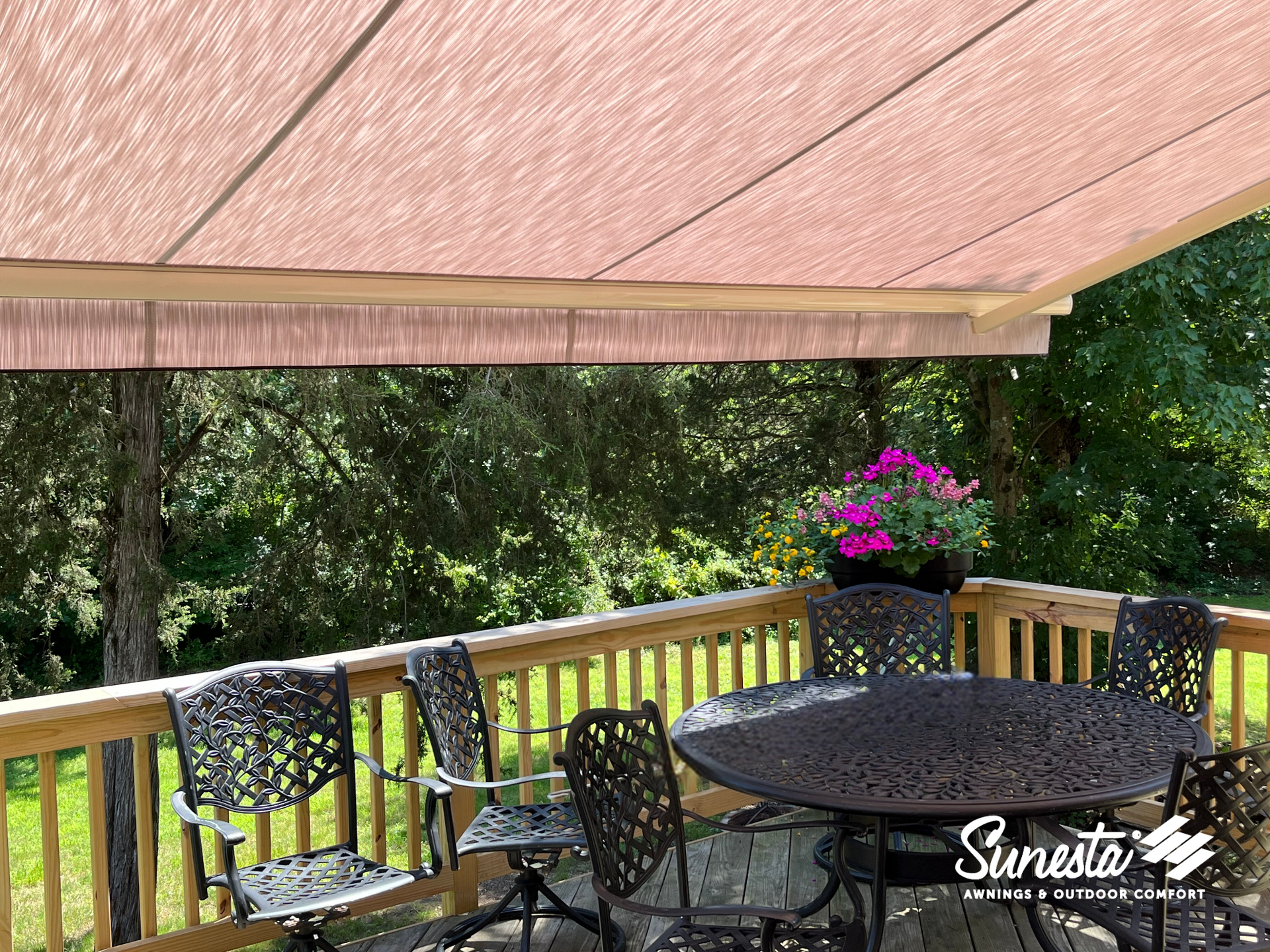 A deck with patio furniture shaded by a retractable, red-brown awning. Lush greenery in the background.