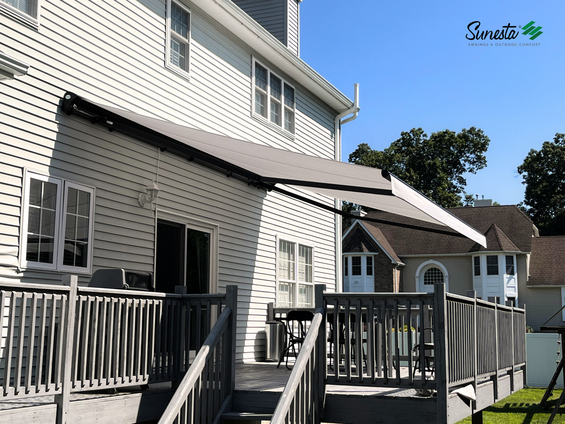 Gray awning extended from a white house over a wooden deck with furniture.