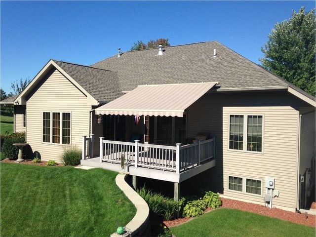 Back view of a house with a deck and retractable awning. Beige siding, green lawn, and blue sky.