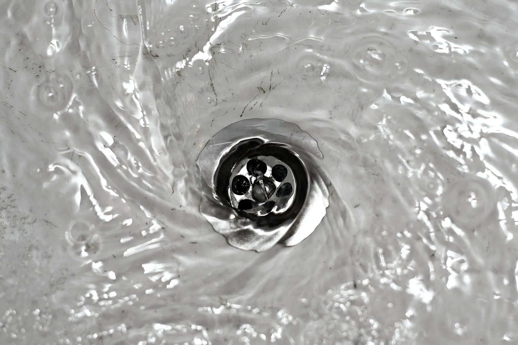A Black and White Photo of Water Running Down a Drain — Vision Plumbing Queensland in Pimlico, QLD
