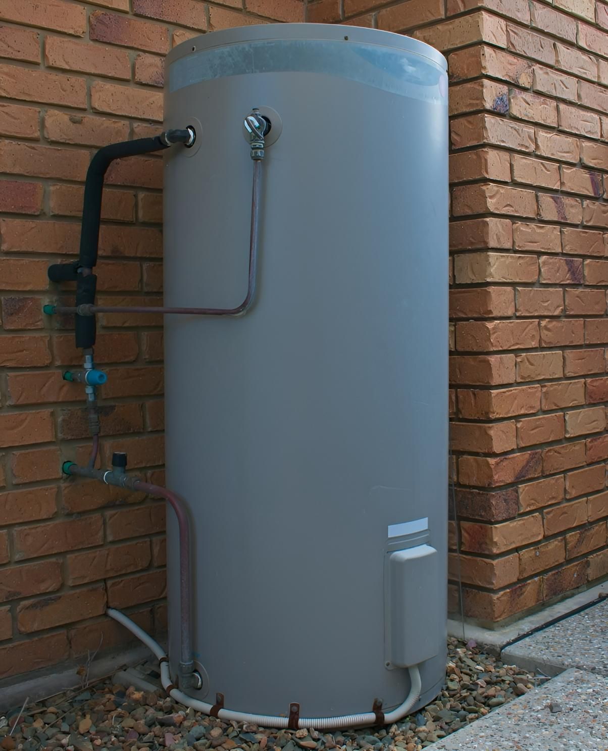 A Large Gray Water Heater is Attached to a Brick Wall — Vision Plumbing Queensland in Pimlico, QLD