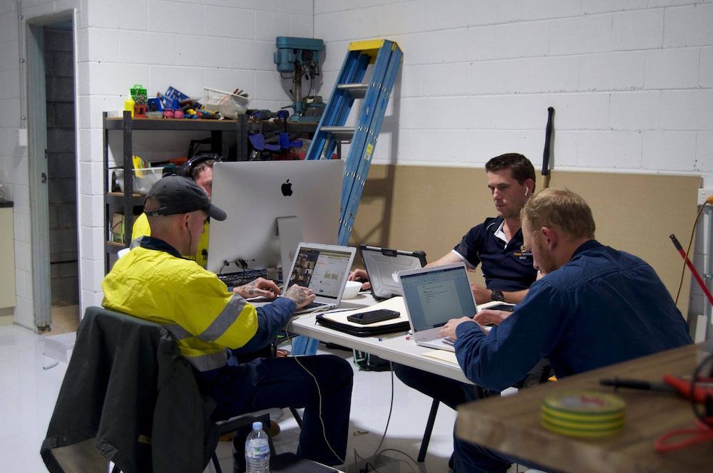 A Group of Men Are Sitting at a Table With Laptops — Central Electrical Group in Gladstone Central, QLD