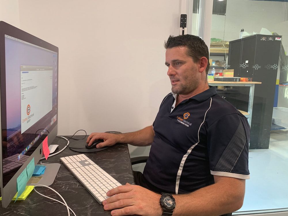 A Man is Sitting at a Desk in Front of a Computer — Central Electrical Group in Gladstone Central, QLD