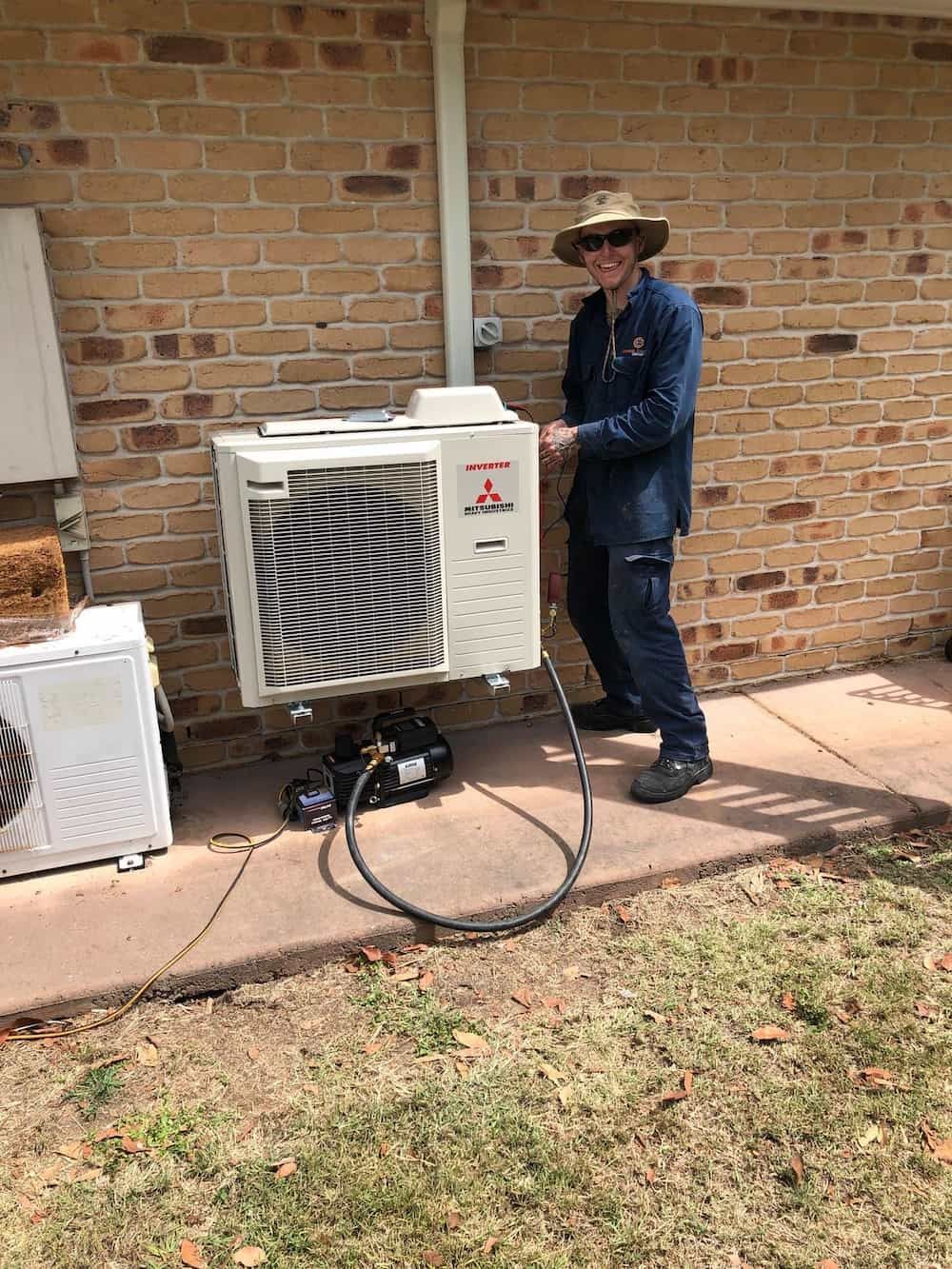 A Man is Working on an Air Conditioner Outside of a Brick Building — Central Electrical Group in Rockhampton, QLD