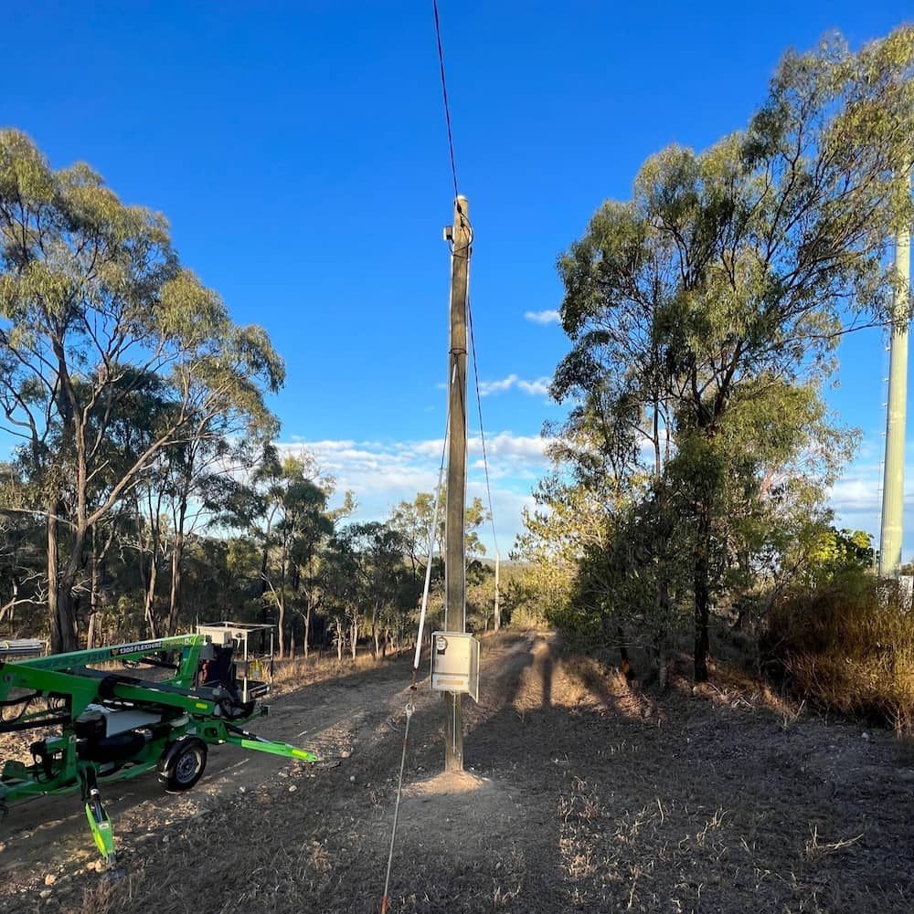 A Green Crane is Sitting Next to a Pole in the Middle of a Field — Central Electrical Group in Gladstone Central, QLD
