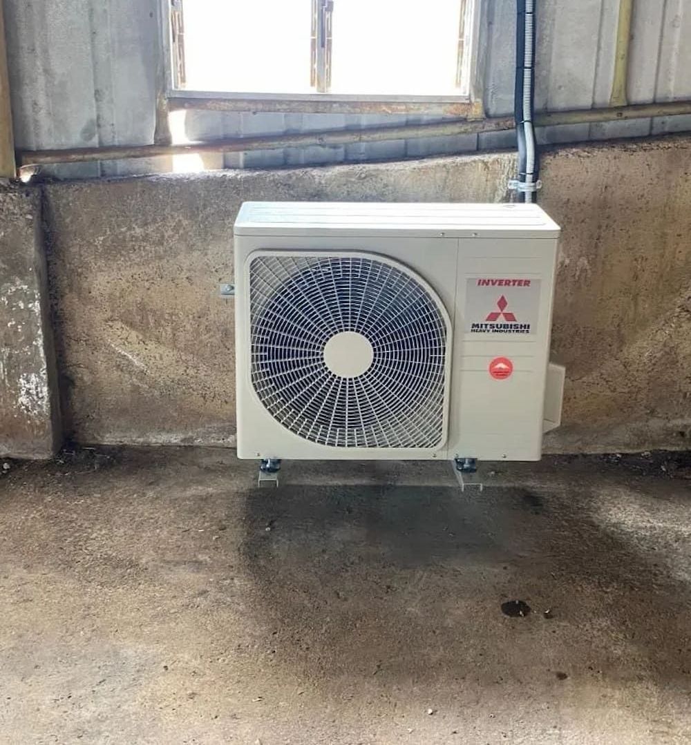 A White Air Conditioner is Hanging on a Wall Next to a Window — Central Electrical Group in Gladstone Central, QLD