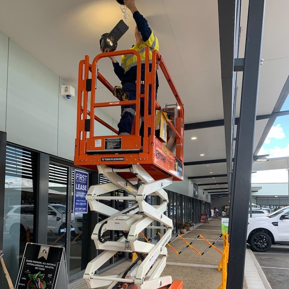 A Man is Standing on a Scissor Lift Working on a Light — Central Electrical Group in Gracemere, QLD