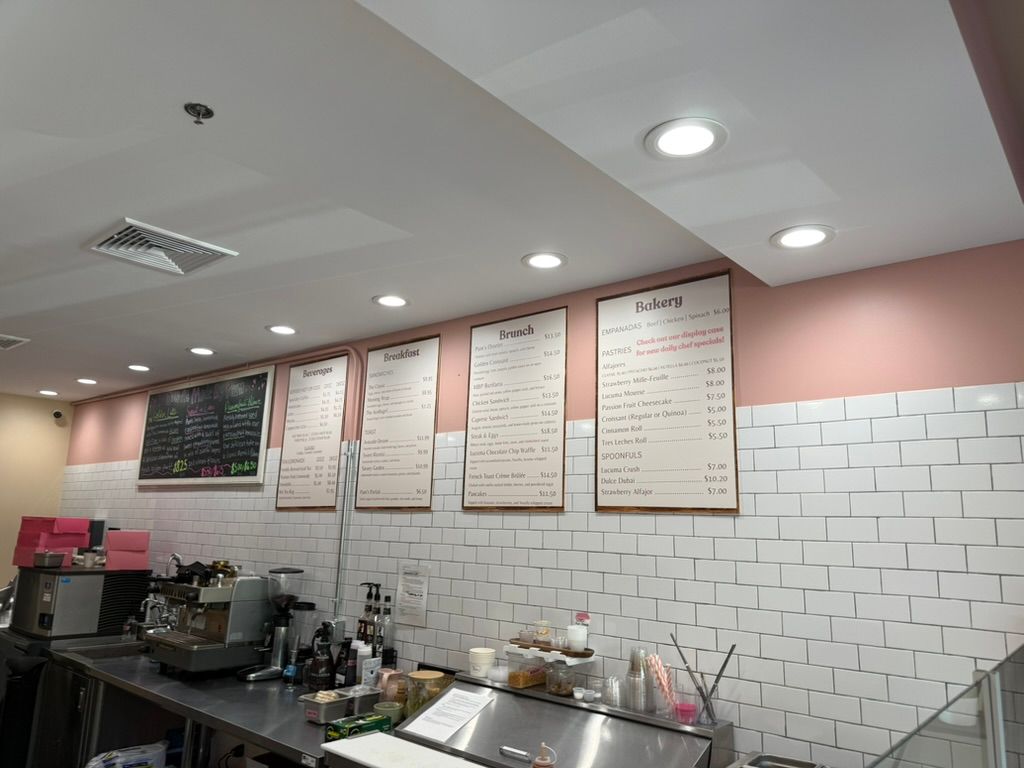 Interior of a cafe with menus on the wall above the counter; white tile and pink accents.