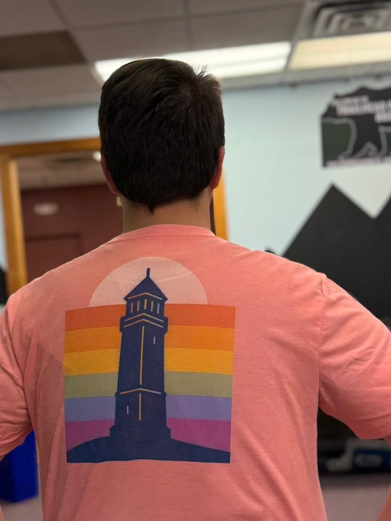 Person wearing a pink t-shirt with a lighthouse design over a rainbow background.