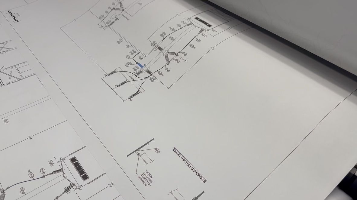 Blueprint document being printed, showing architectural plans with black lines on white paper.
