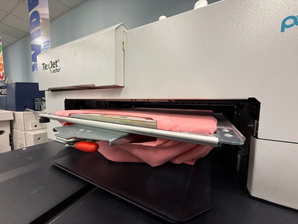 A white digital printer printing on a pink t-shirt, inside a store.