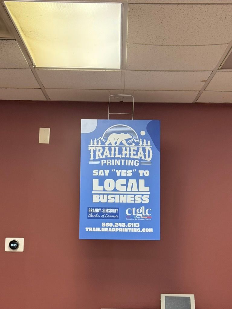 Sign for Trailhead Printing on a maroon wall, encouraging support of local businesses.