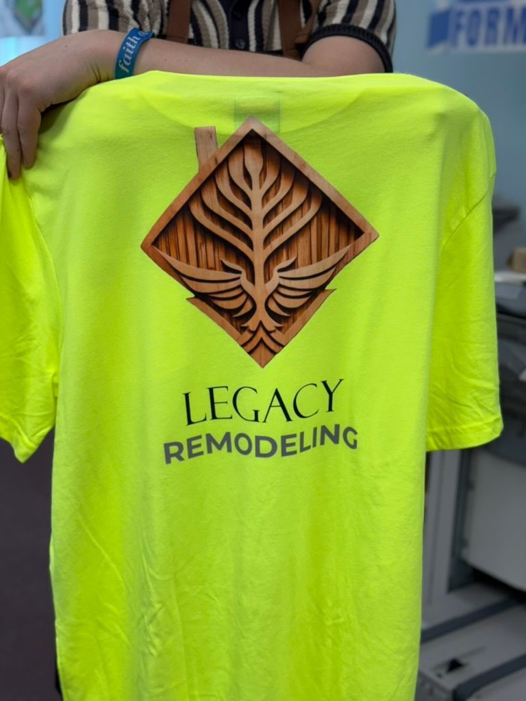 Yellow Legacy Remodeling t-shirt with a wood-like logo held by a person.