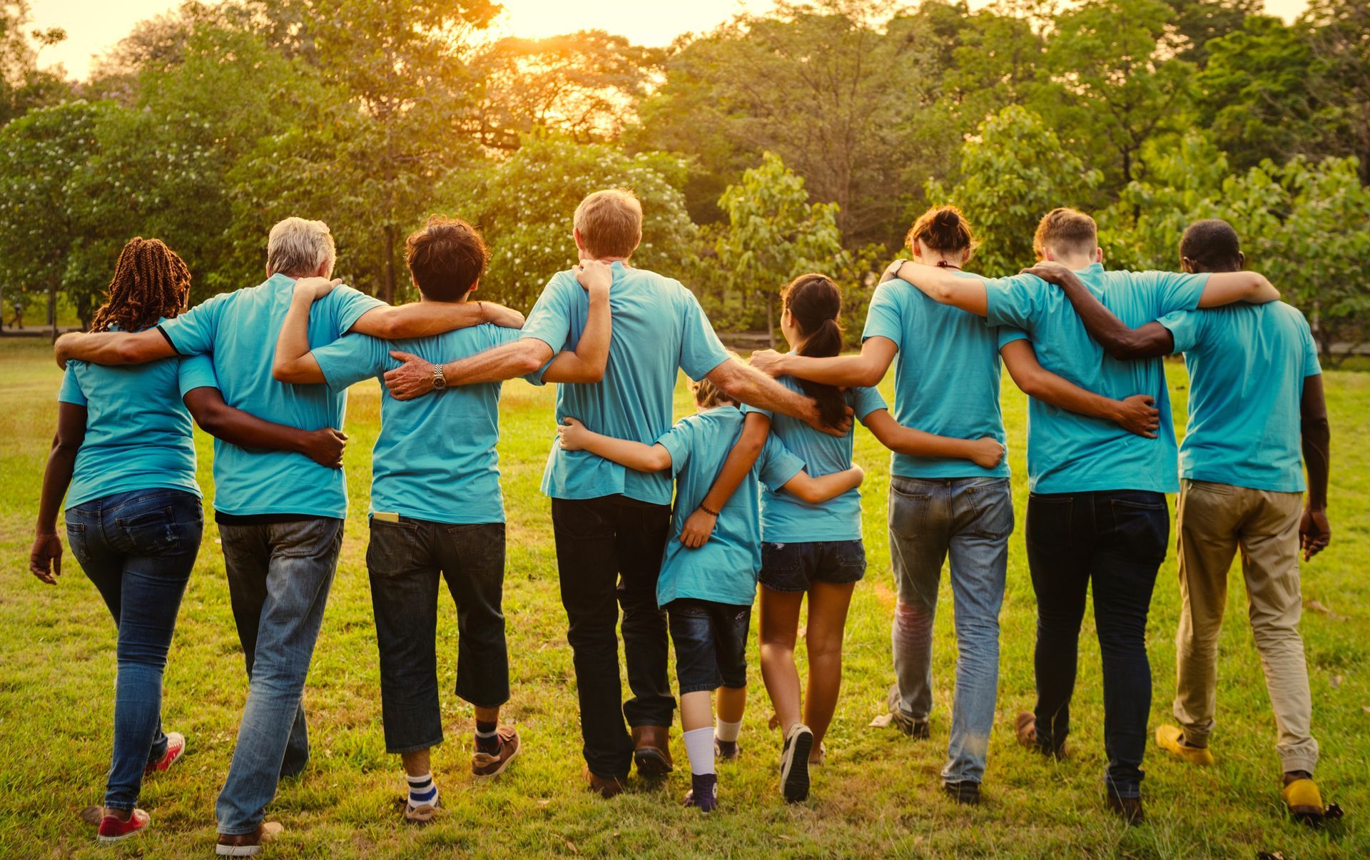 Group of people in matching blue shirts walking arm-in-arm through a sunny park