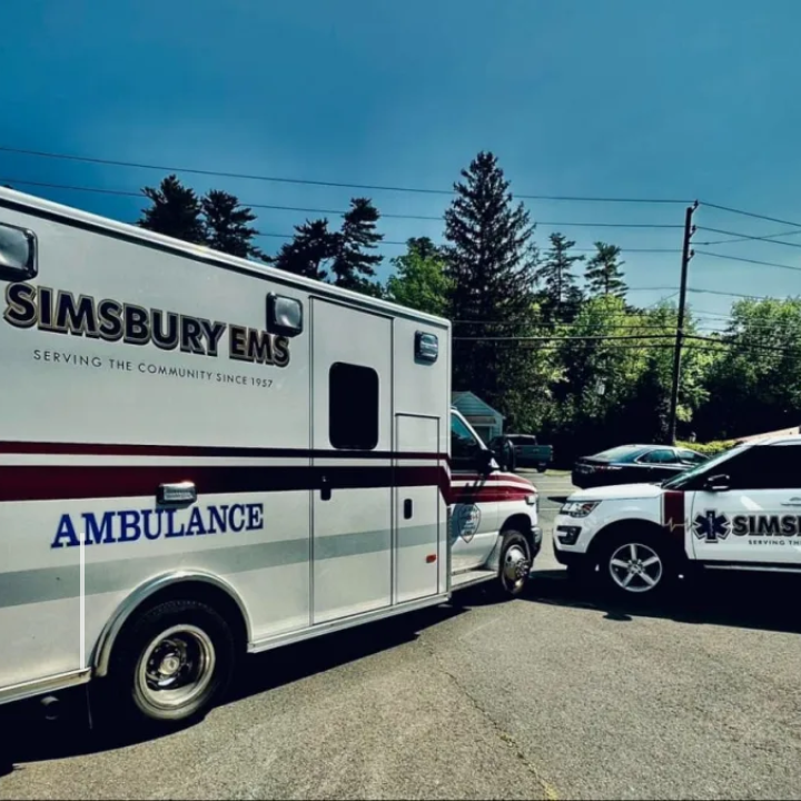 White and red Simsbury EMS ambulance and SUV parked outdoors on a sunny day.